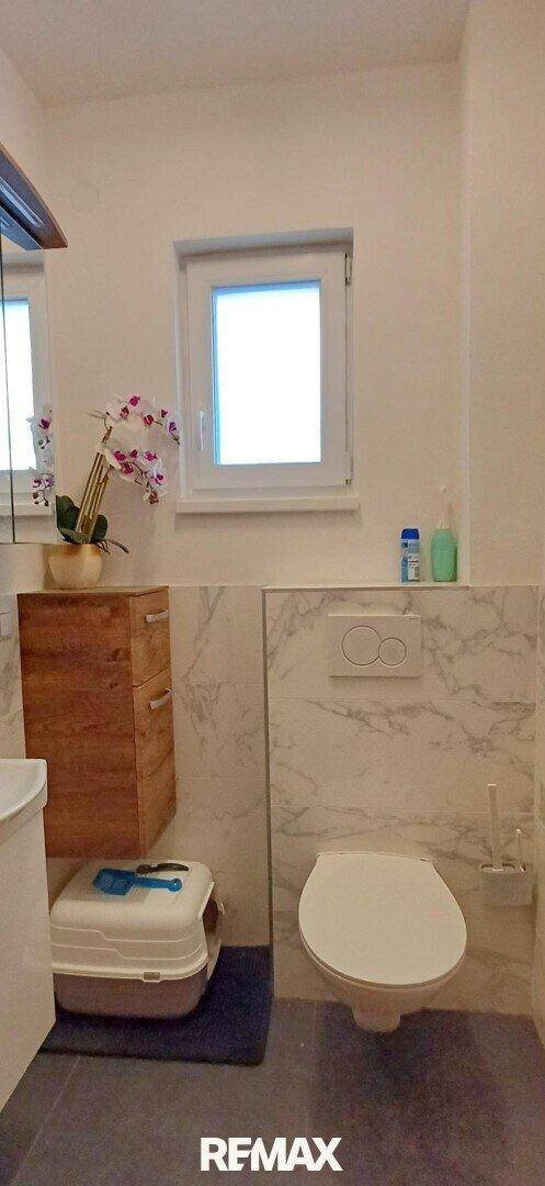 Modernes Gäste-WC mit Wand-WC, Fenster und Marmoroptik-Fliesen an den Wänden.
