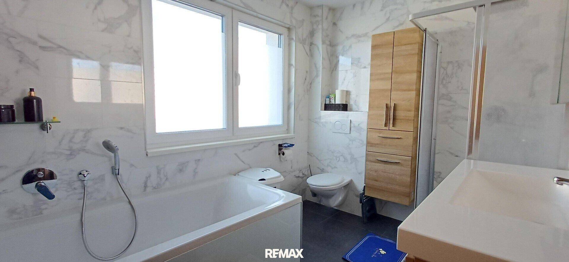 Helles Badezimmer mit Badewanne, Dusche, WC und modernen Marmoroptik-Fliesen.