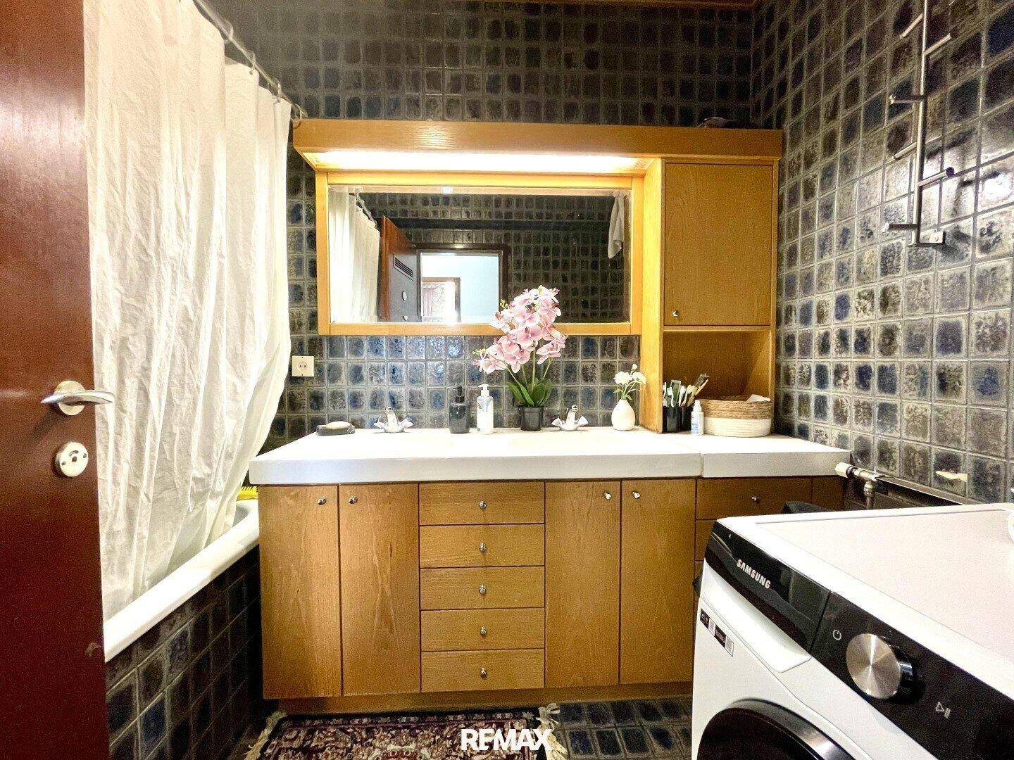 Badezimmer mit Badewanne, Waschbecken und dunklen Fliesen im Retro-Stil.