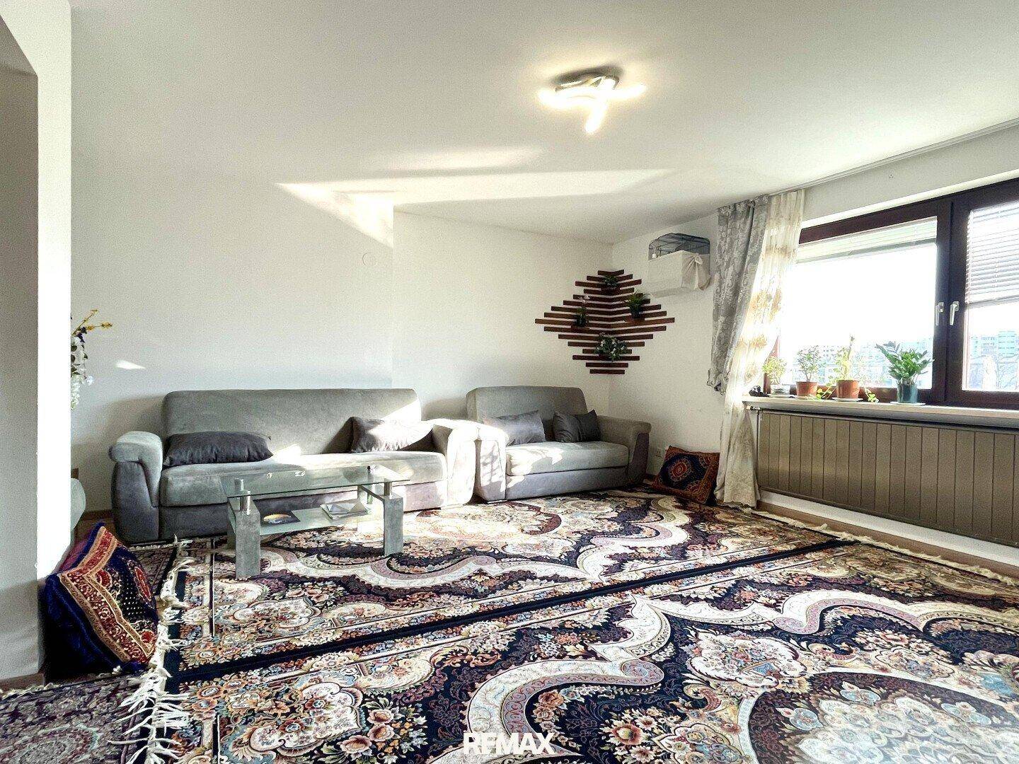 Helles Wohnzimmer mit großem Teppich, bequemen Sofas und Fenster mit Tageslicht.