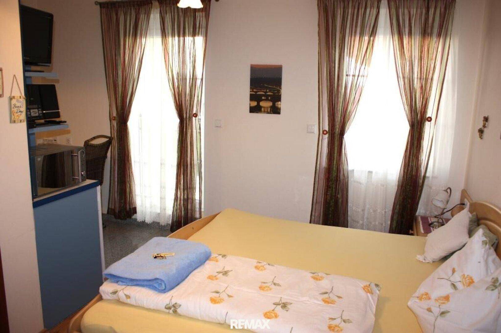 Schlafzimmer mit Doppelbett, Fernseher und Zugang zu einem kleinen Balkon oder Terrasse.