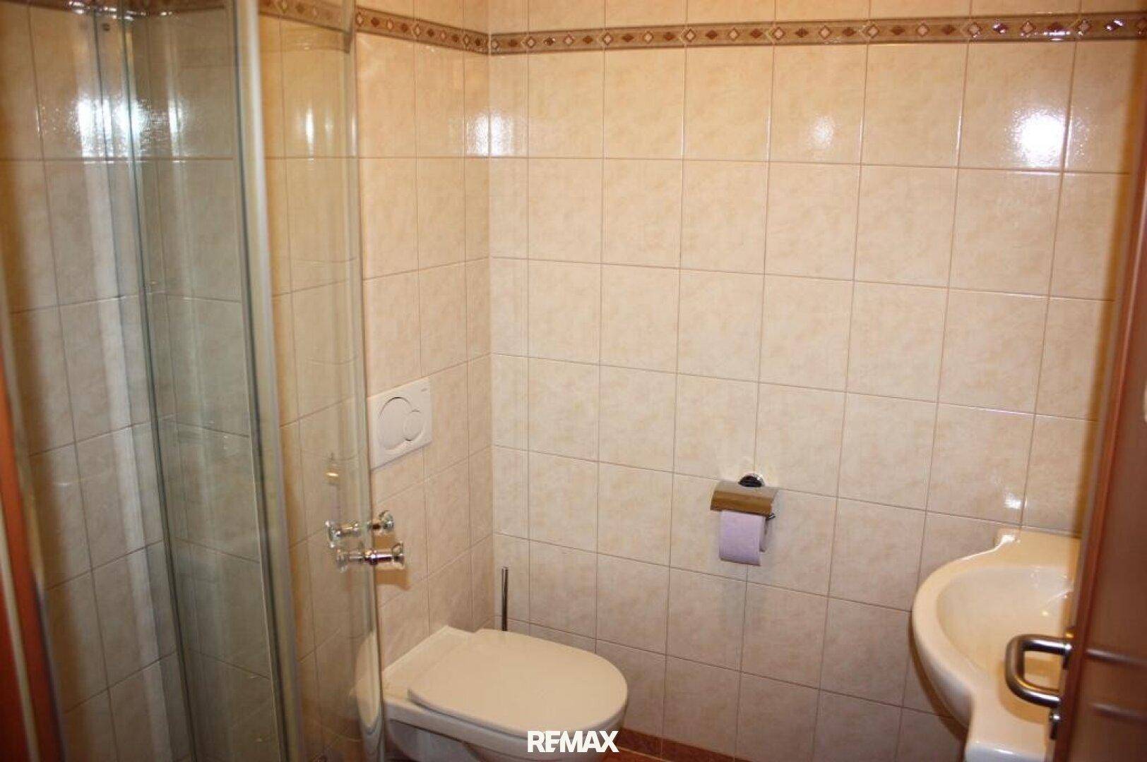 Gefliestes Badezimmer mit Duschkabine, Toilette und Waschbecken in hellem Design.