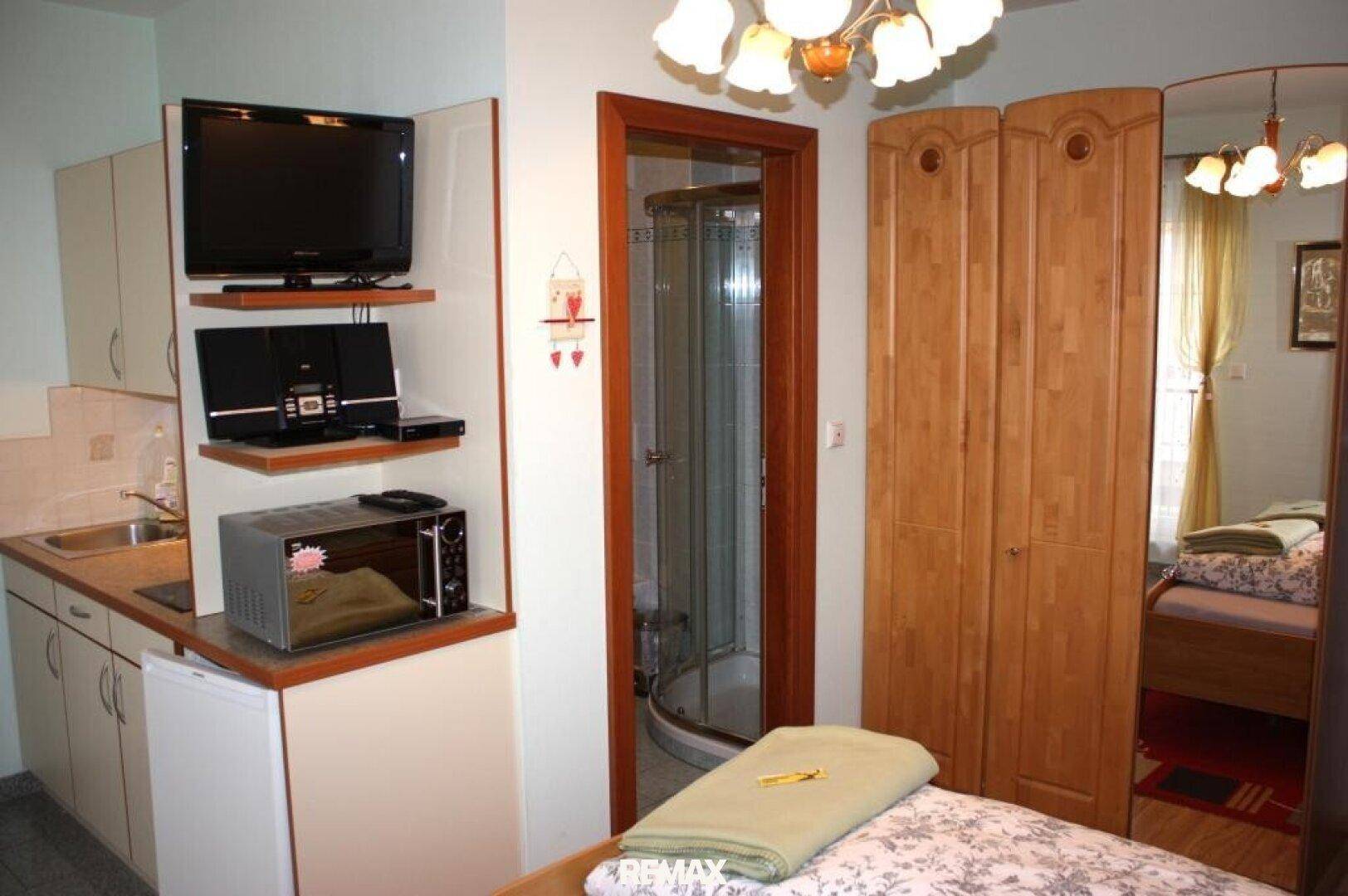 Schlafzimmer mit Doppelbett, Kleiderschrank und integrierter Küchenzeile mit Mikrowelle.