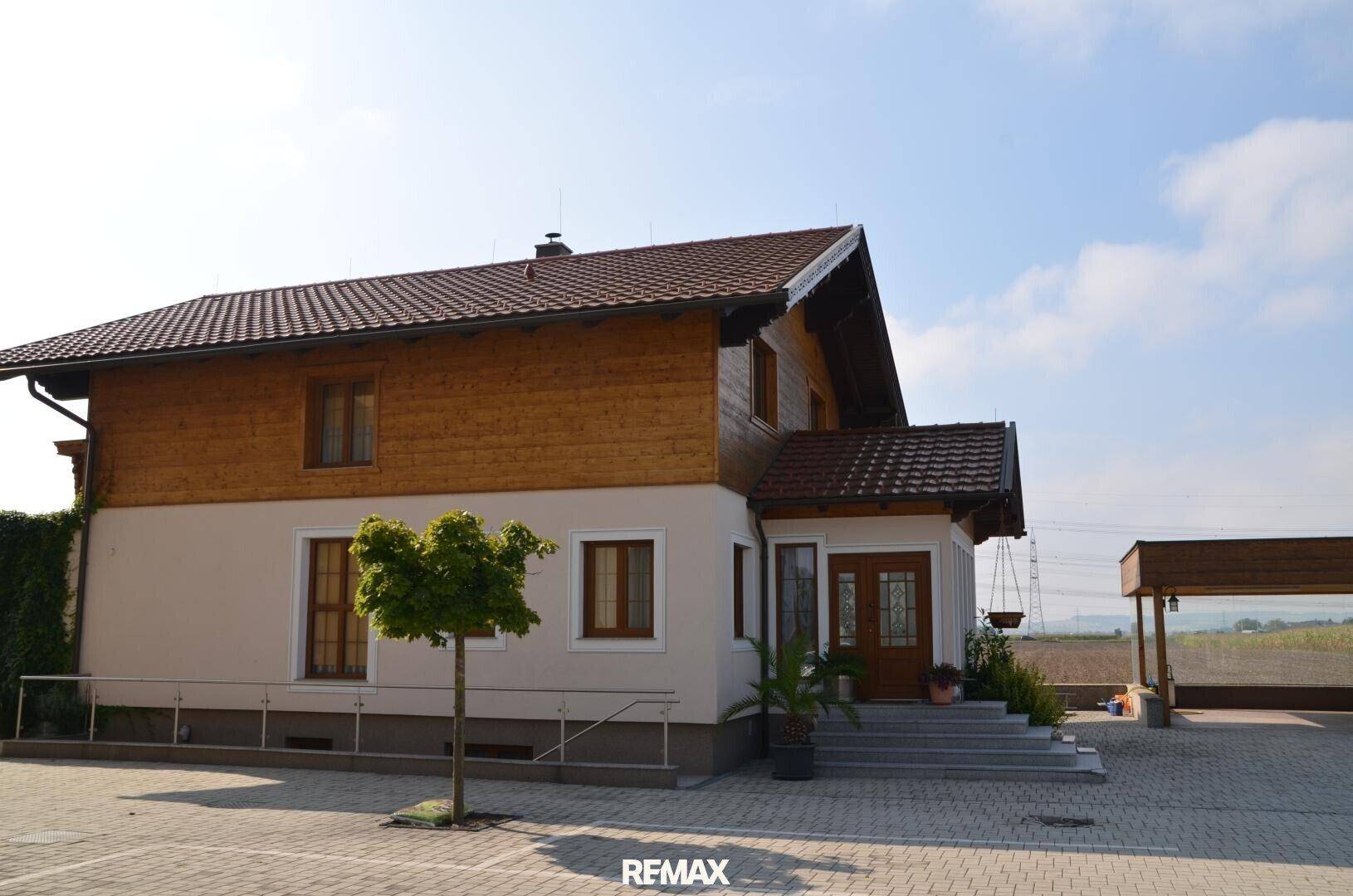 Ansicht eines gepflegten Landhauses mit Holzelementen und großzügigem Vorplatz, umgeben von Natur.