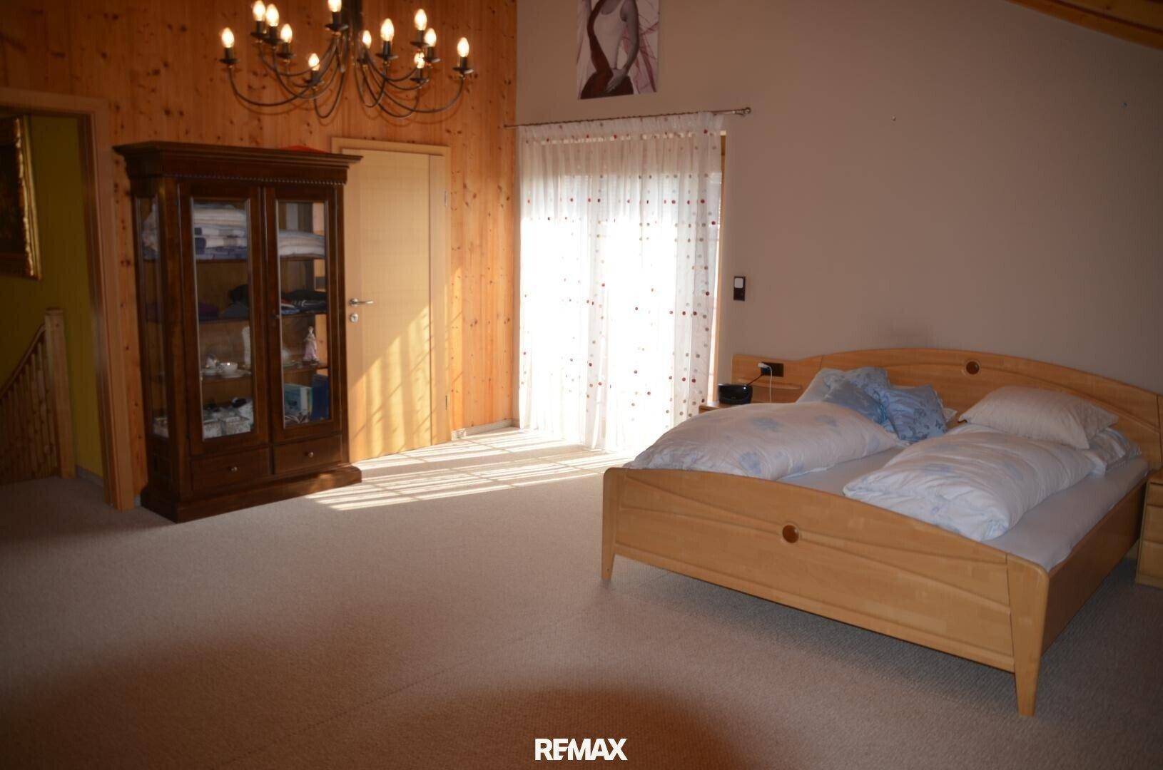 Gemütliches Schlafzimmer mit Holzwänden, Teppichboden und einem großen Fenster, das viel Licht hereinlässt.