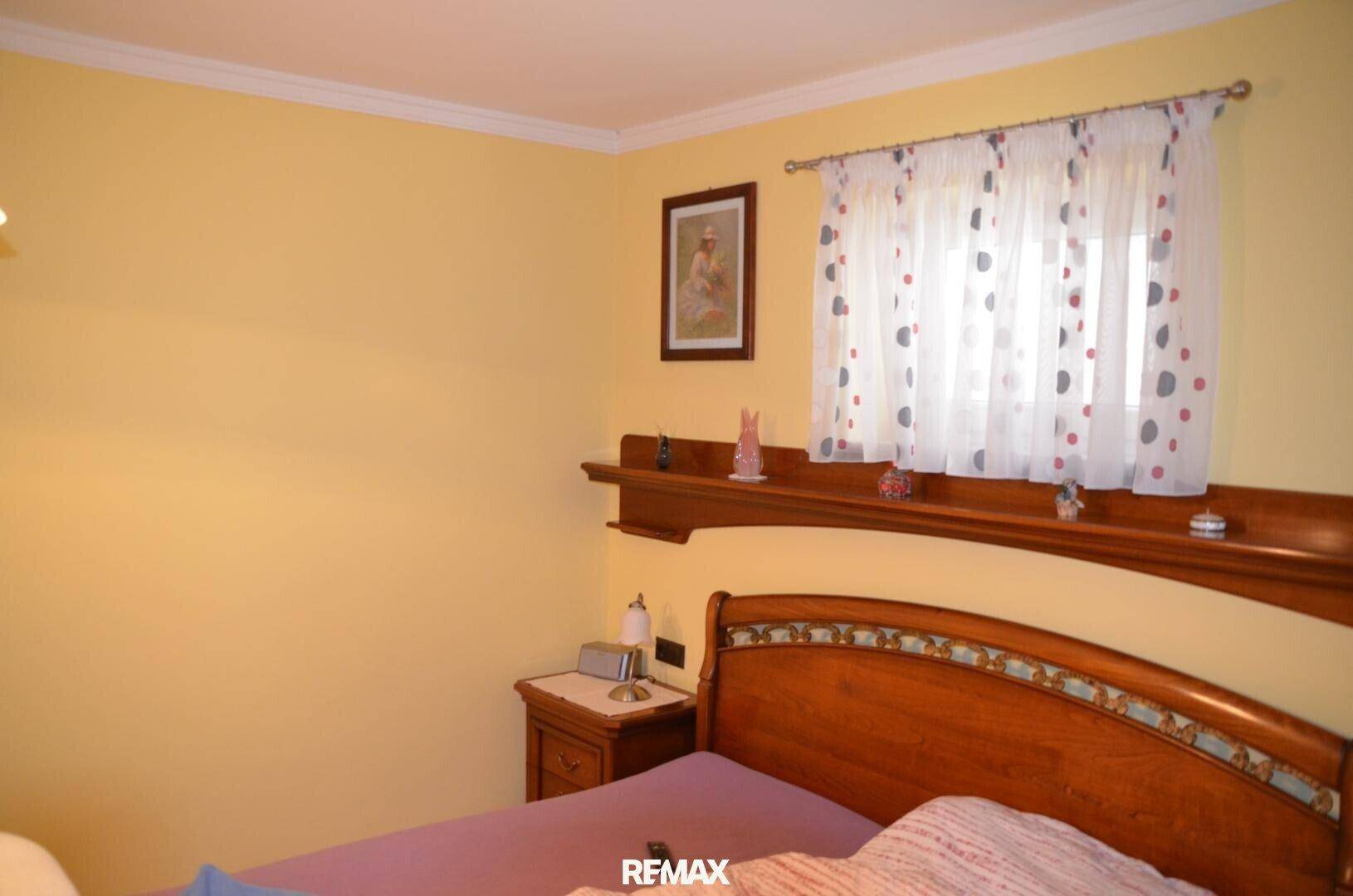 Schlafzimmer mit gelben Wänden, Holzbett und einem Fenster mit Vorhängen.