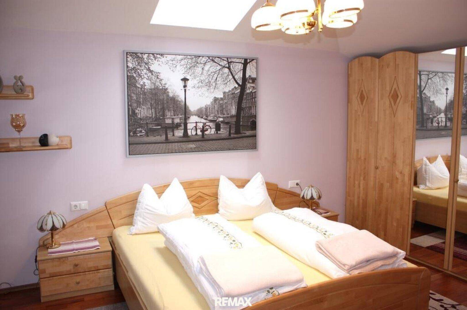 Gemütliches Schlafzimmer mit Holzmöbeln, Dachfenster und einem großen Wandbild über dem Bett.
