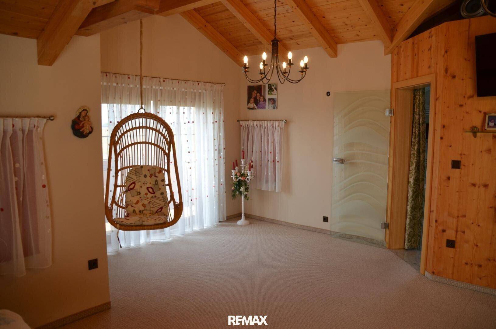 Großes Schlafzimmer mit Holzbalkendecke, Schaukelstuhl und viel natürlichem Licht.