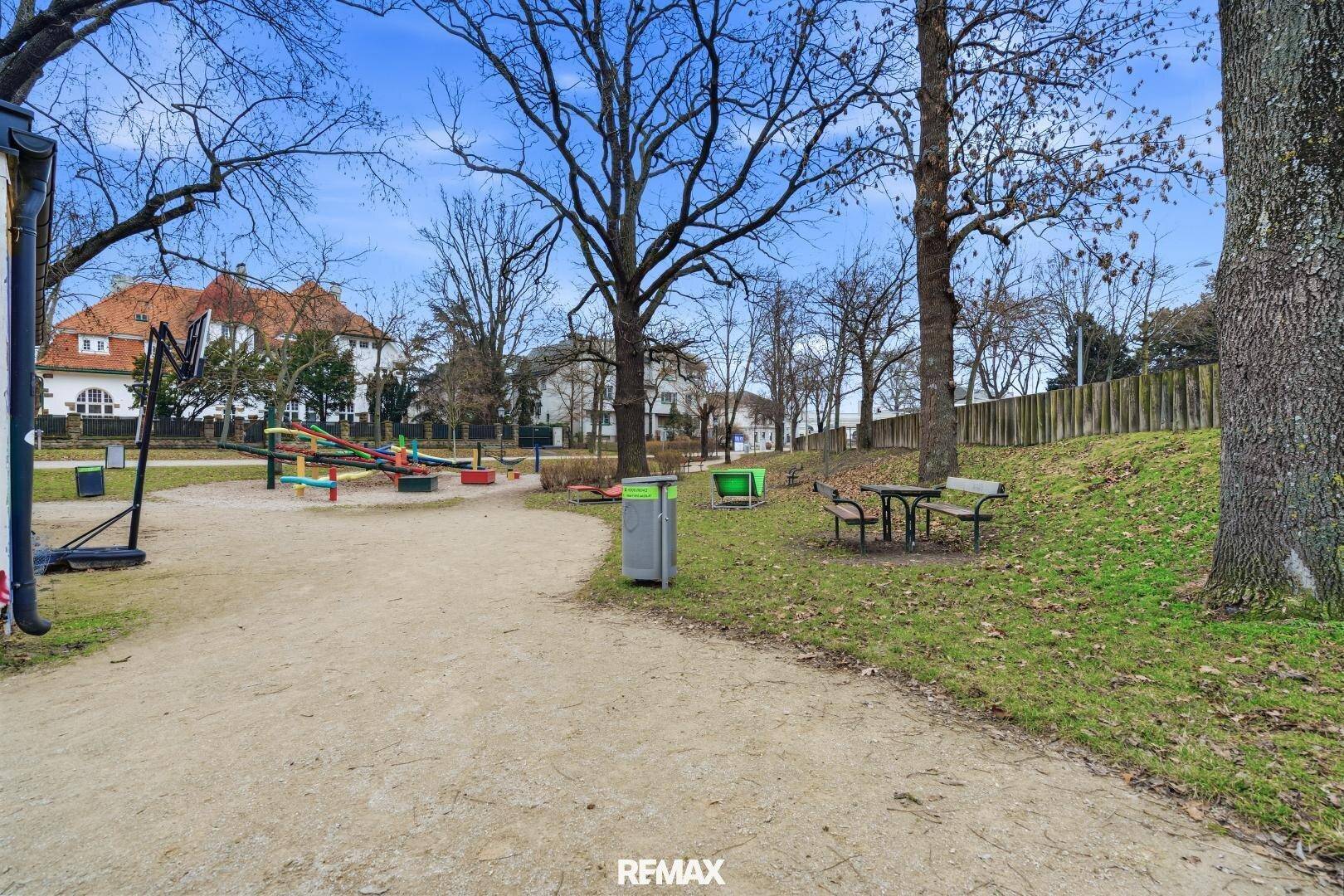 Kinderspielplatz in einer grünen Parkanlage mit Bäumen und Sitzgelegenheiten für Familien.