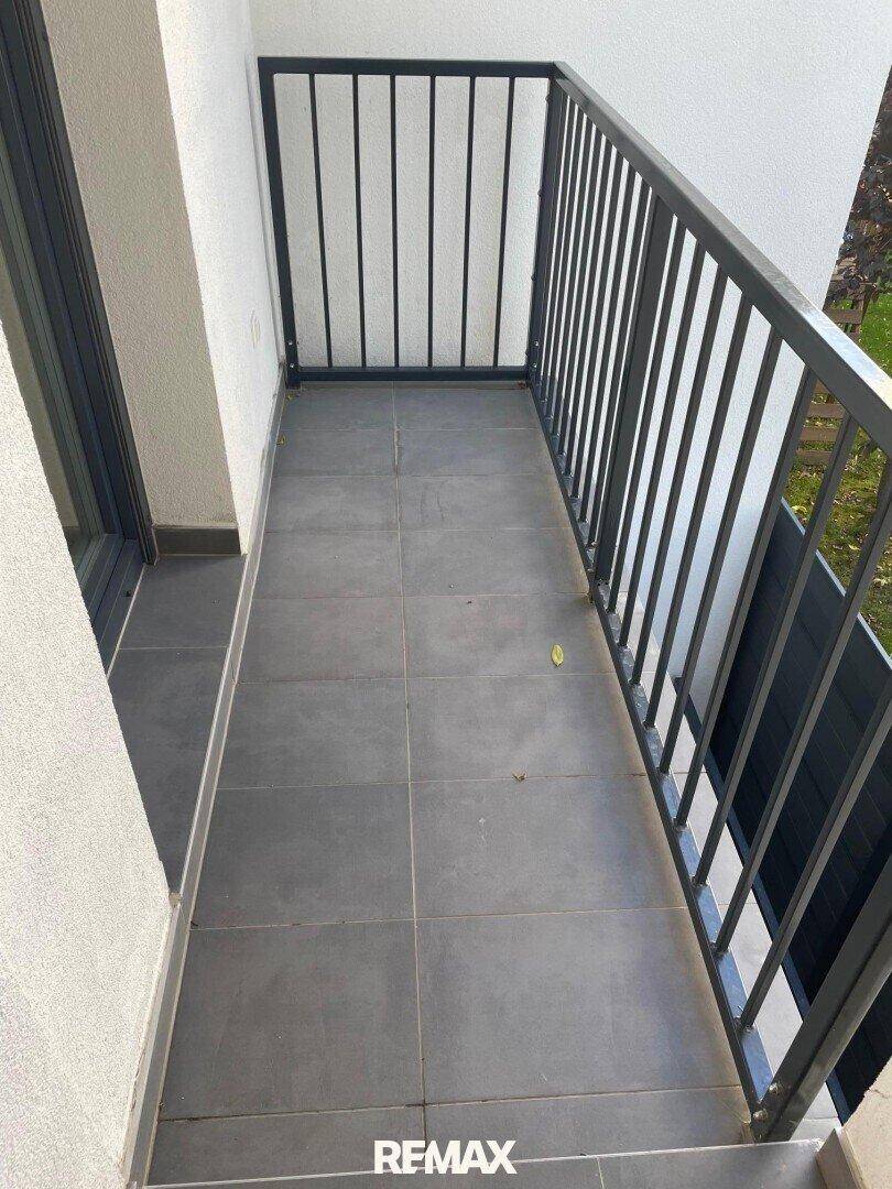 Heller Balkon mit grauen Fliesen und modernem Metallgeländer, bereit zur individuellen Gestaltung.