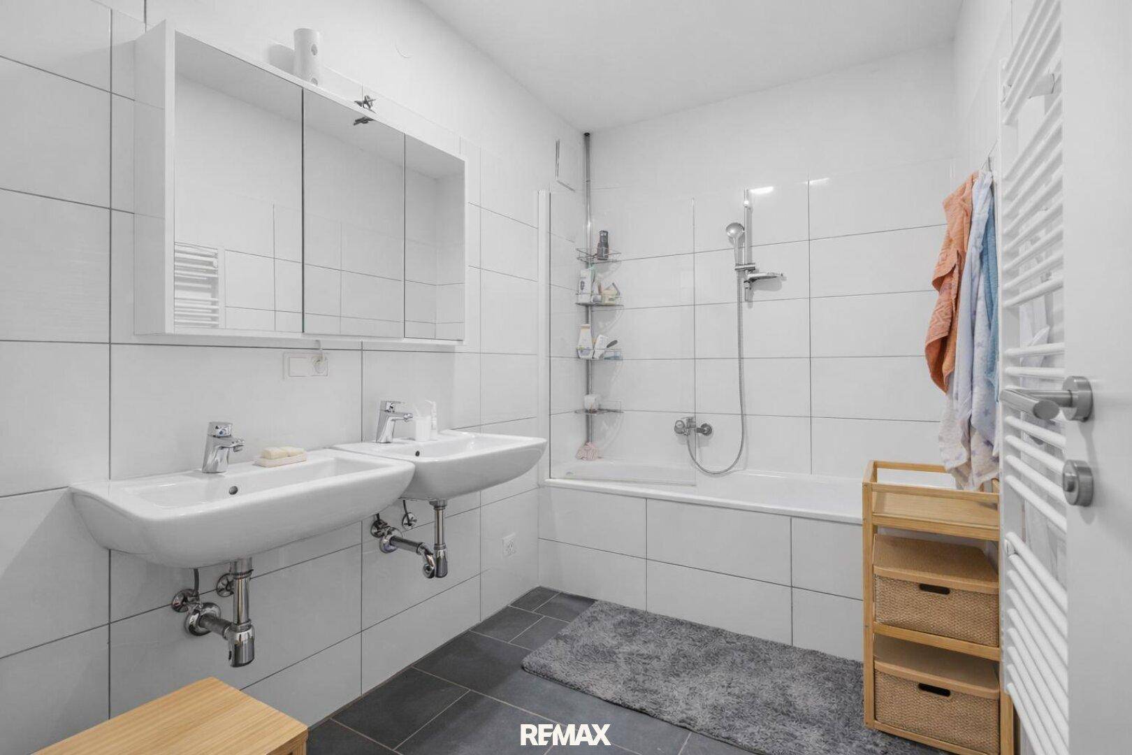 Modernes Badezimmer mit Doppelwaschbecken, Badewanne mit Duschfunktion und beheiztem Handtuchhalter.