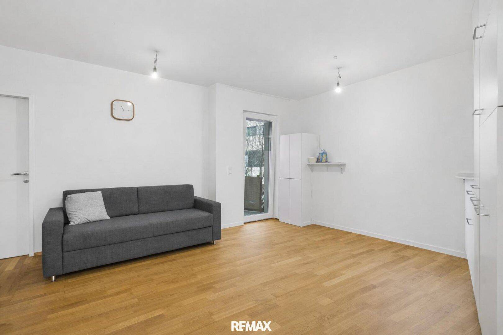 Helles Wohnzimmer mit grauem Sofa, Holzboden und Zugang zu einem sonnigen Balkon.