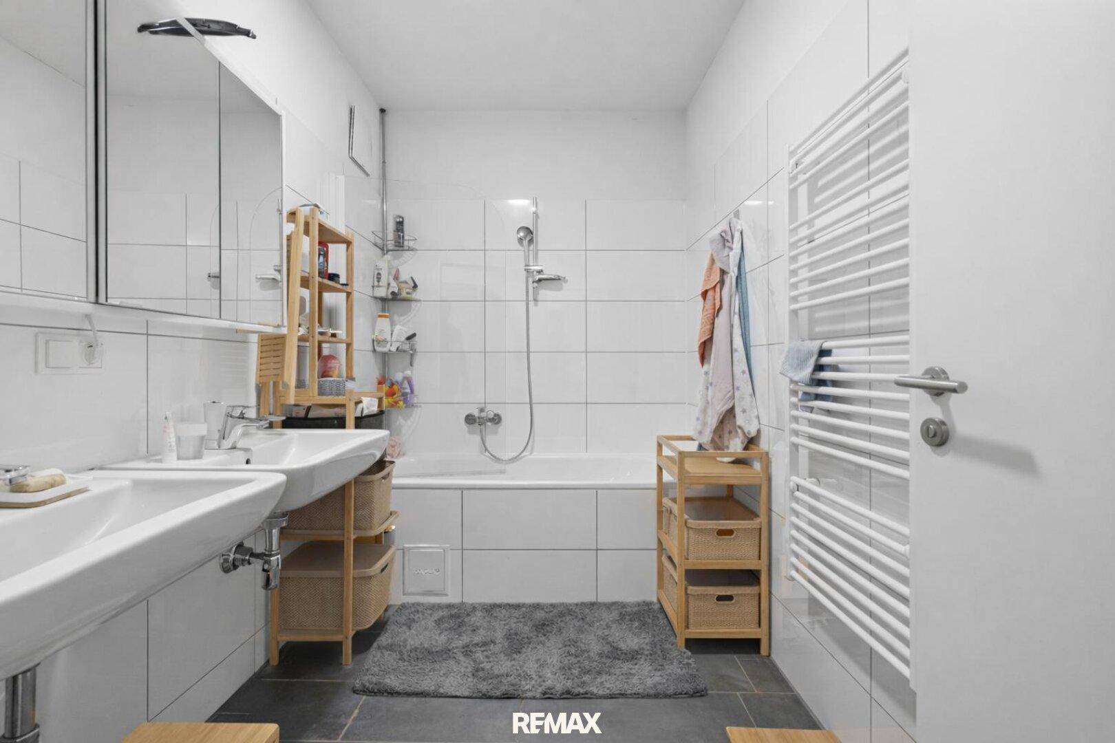 Helles Badezimmer mit weißen Fliesen, zwei Waschbecken und Badewanne mit Duschfunktion.