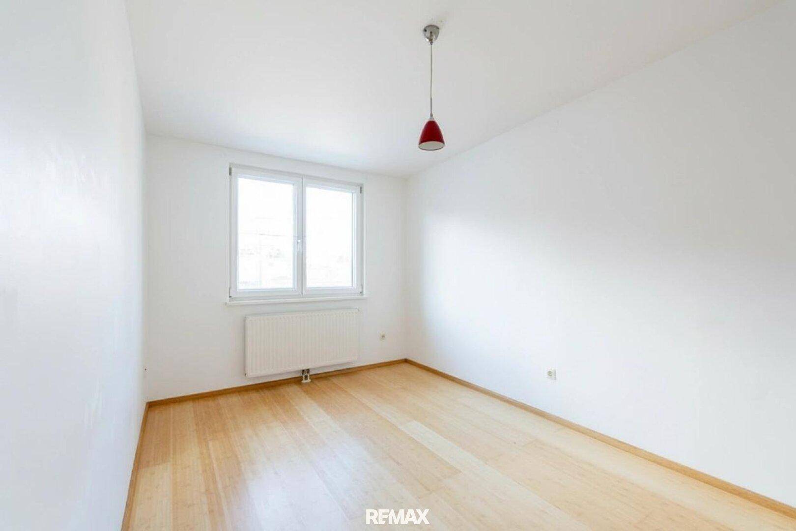 Helles Zimmer mit Holzfußboden und großem Fenster, ideal als Schlaf- oder Kinderzimmer.