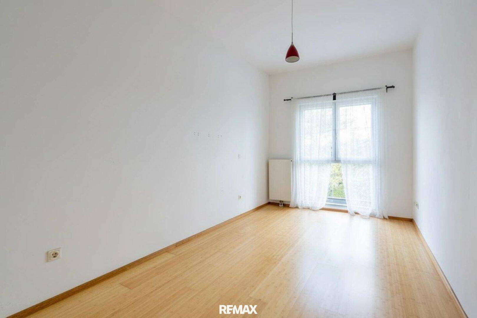 Helles Zimmer mit Holzfußboden und großem Fenster, ideal als Schlaf- oder Arbeitszimmer.
