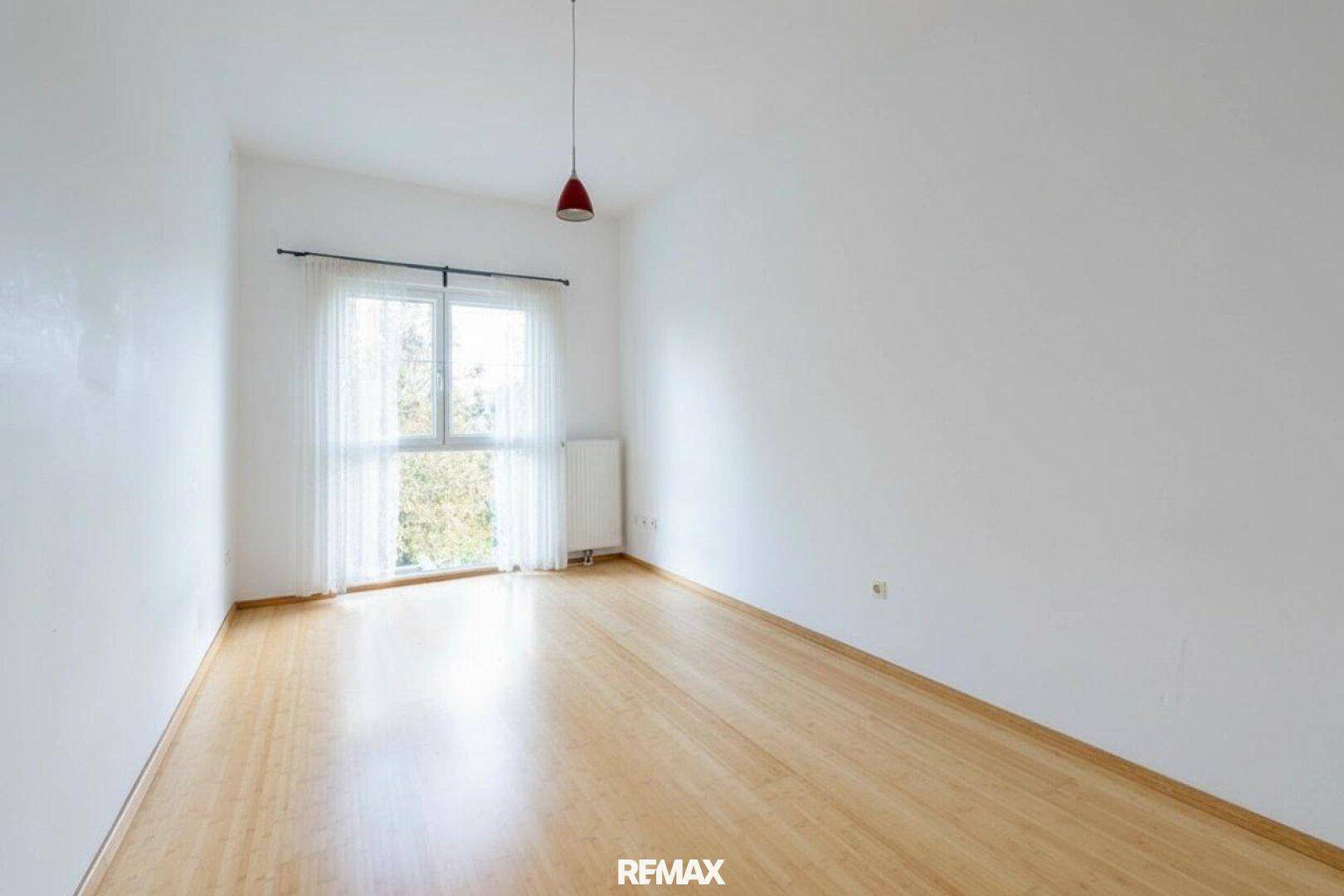 Helles Zimmer mit Holzfußboden und Fenster, das viel Tageslicht hereinlässt.