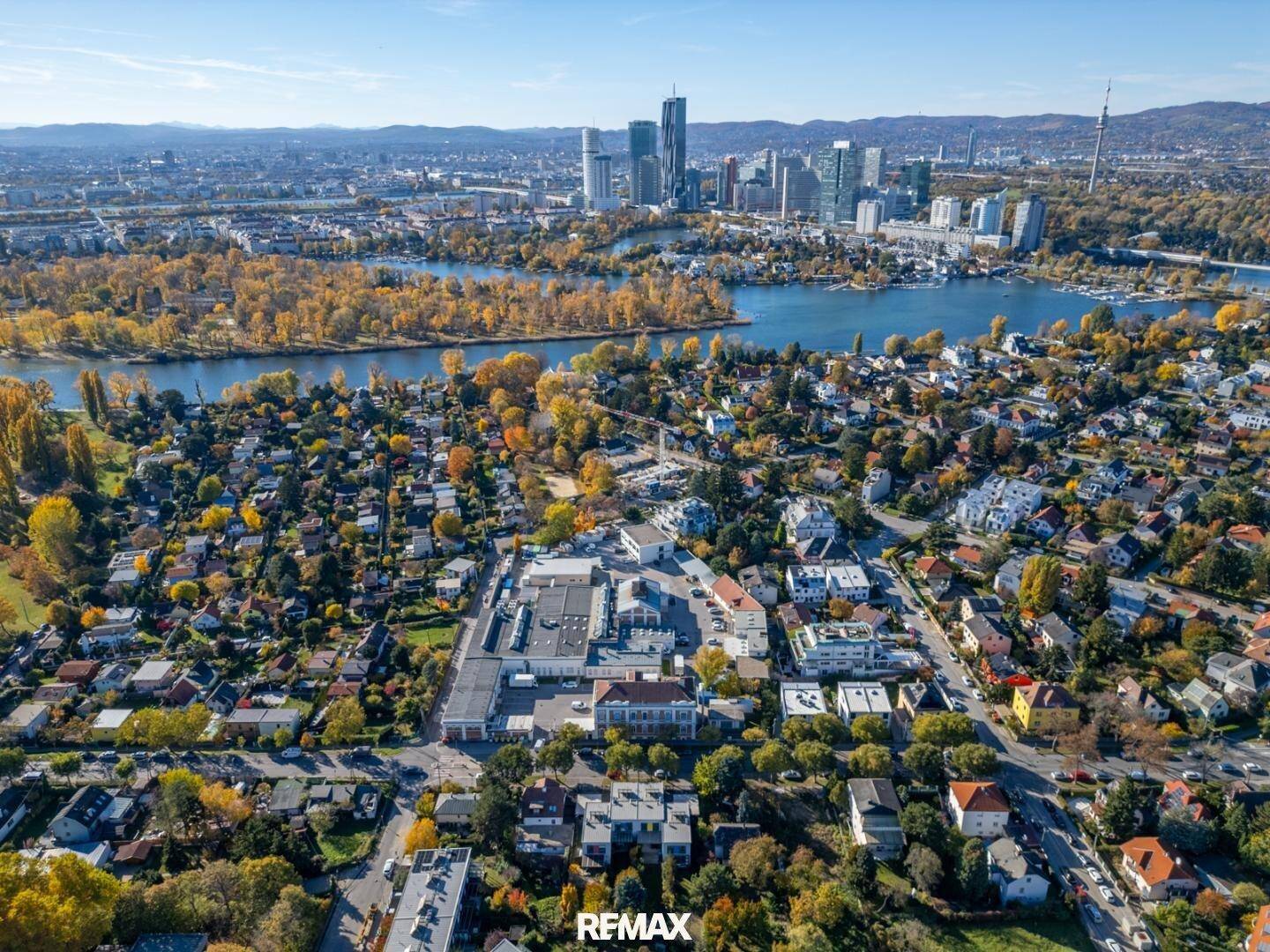 Weitläufige Luftaufnahme einer Stadtlandschaft mit Fluss, Gebäuden und herbstlicher Vegetation.