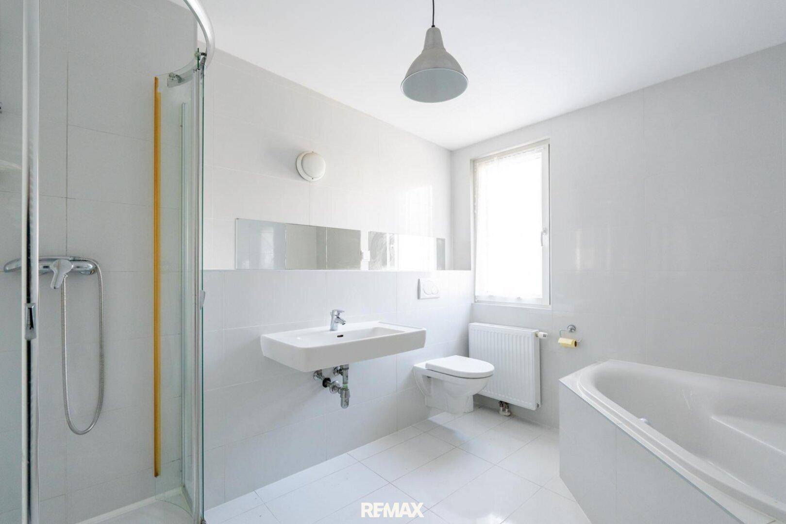 Modernes Badezimmer mit weißen Fliesen, Dusche, Badewanne und Fenster für Tageslicht.