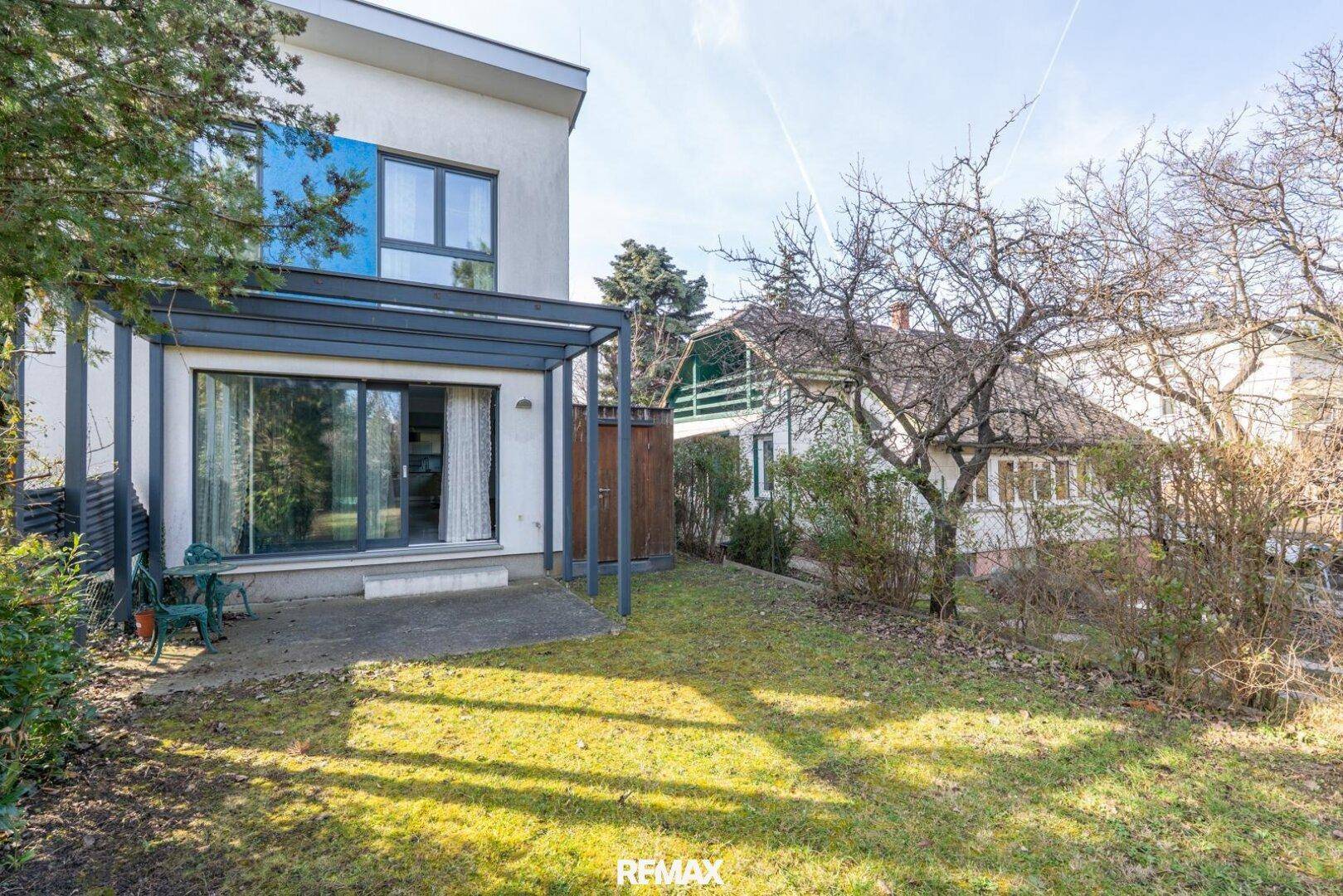 Hinterhof mit kleiner Terrasse, Rasenfläche und Bäumen, ideal für Entspannung im Freien.