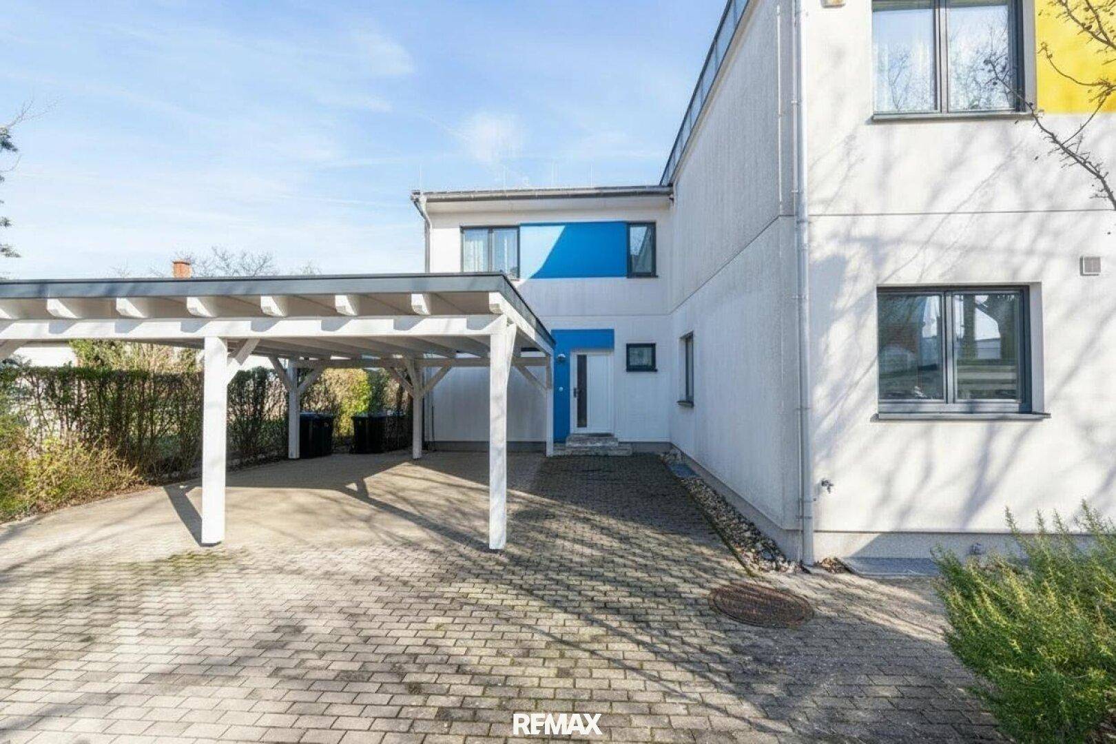 Eingangsbereich des Hauses mit Carport und gepflasterter Auffahrt unter blauem Himmel.
