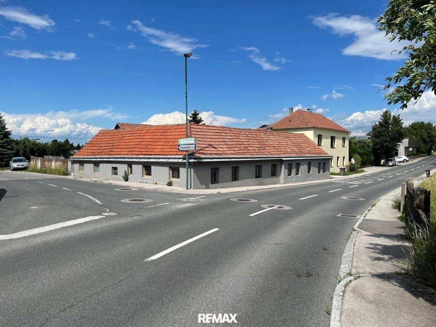 Älteres Gebäude mit rotem Ziegeldach an einer Straßenkreuzung in ländlicher Gegend.