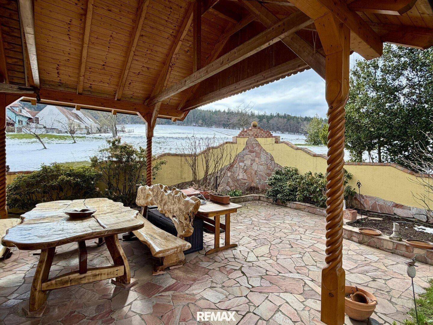 Überdachte Terrasse mit rustikalen Holzmöbeln und Blick auf eine verschneite Landschaft.