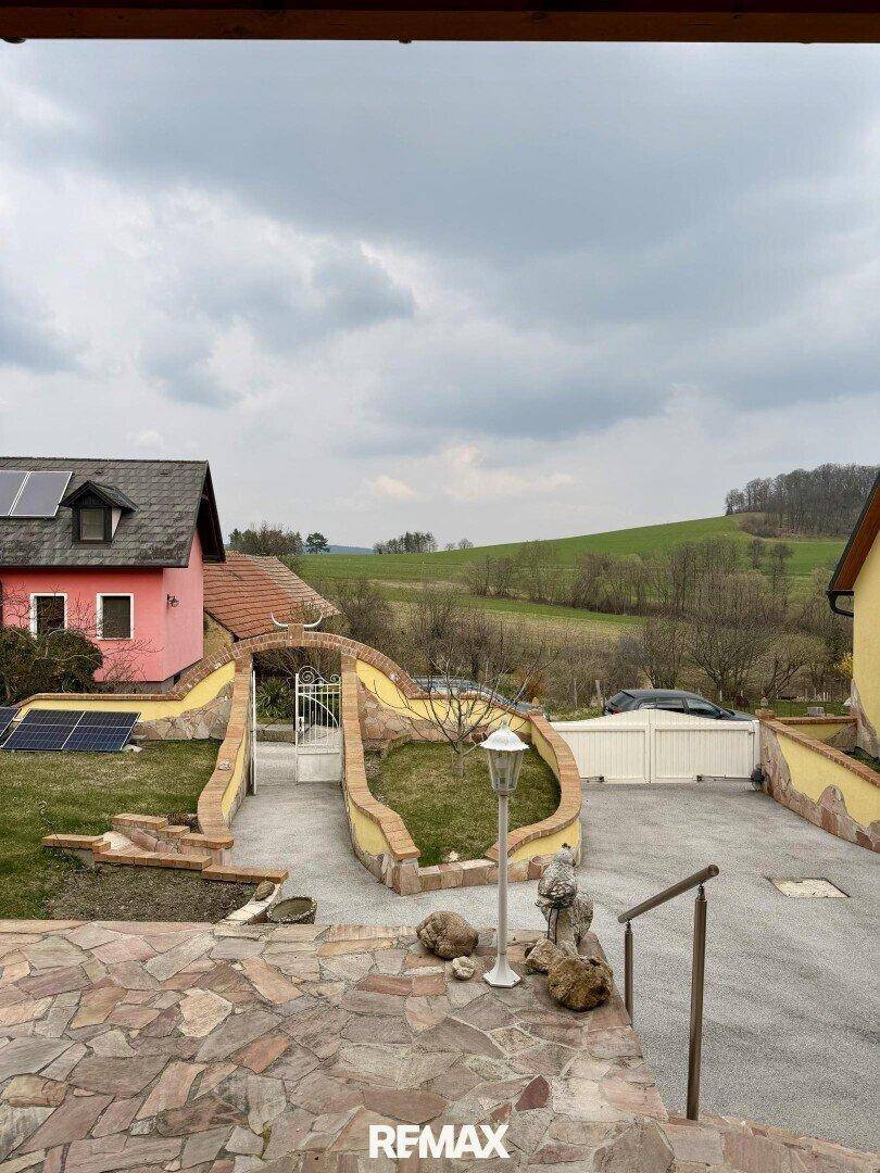 Einfahrt und Vorgartenbereich mit gepflasterten Wegen und Blick auf die grüne Landschaft.