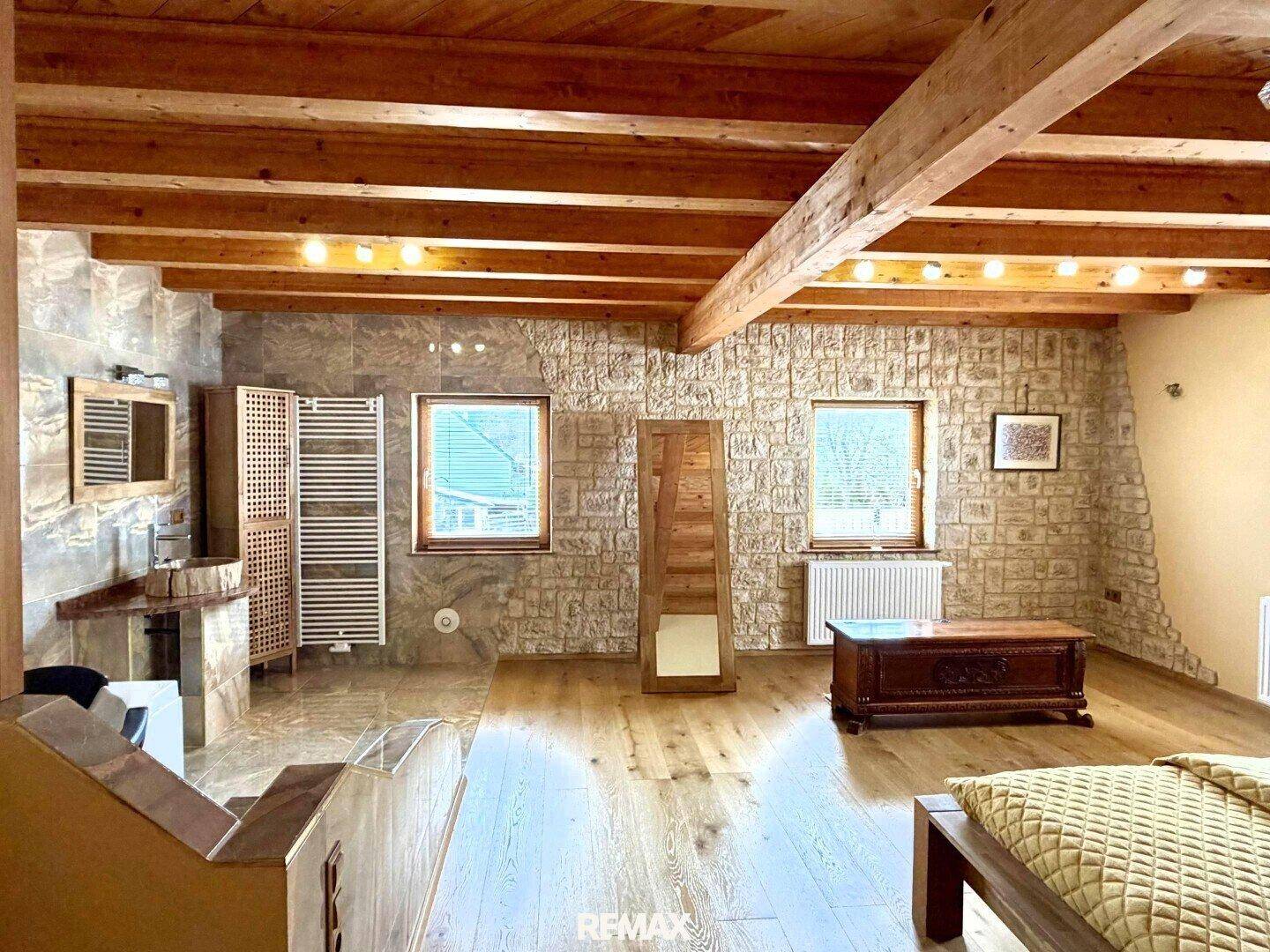 Offener Schlafbereich mit Holzboden, Steinwand und angrenzendem Badezimmerbereich.