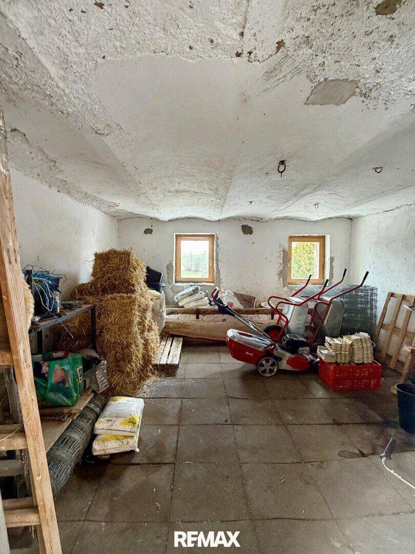 Lagerraum in einer Scheune mit Heuballen, Gartengeräten und einfachen Fenstern.