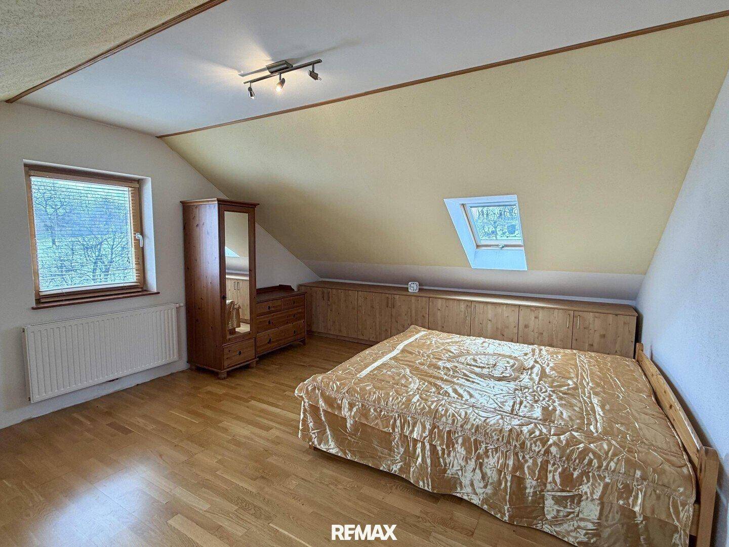 Schlafzimmer im Dachgeschoss mit Holzboden, Dachschräge und eingebauten Schränken.