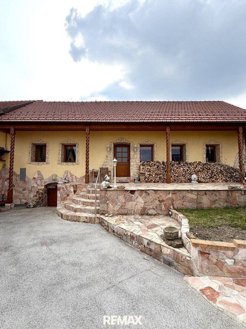 Traditionelles Wohnhaus mit Steinfassade, Holzveranda und gestapeltem Brennholz vor dem Eingang.