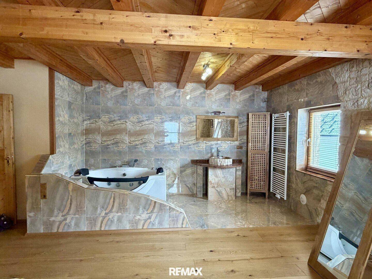 Geräumiges Badezimmer mit Whirlpool-Badewanne, Doppelwaschbecken und Fliesen in Natursteinoptik.