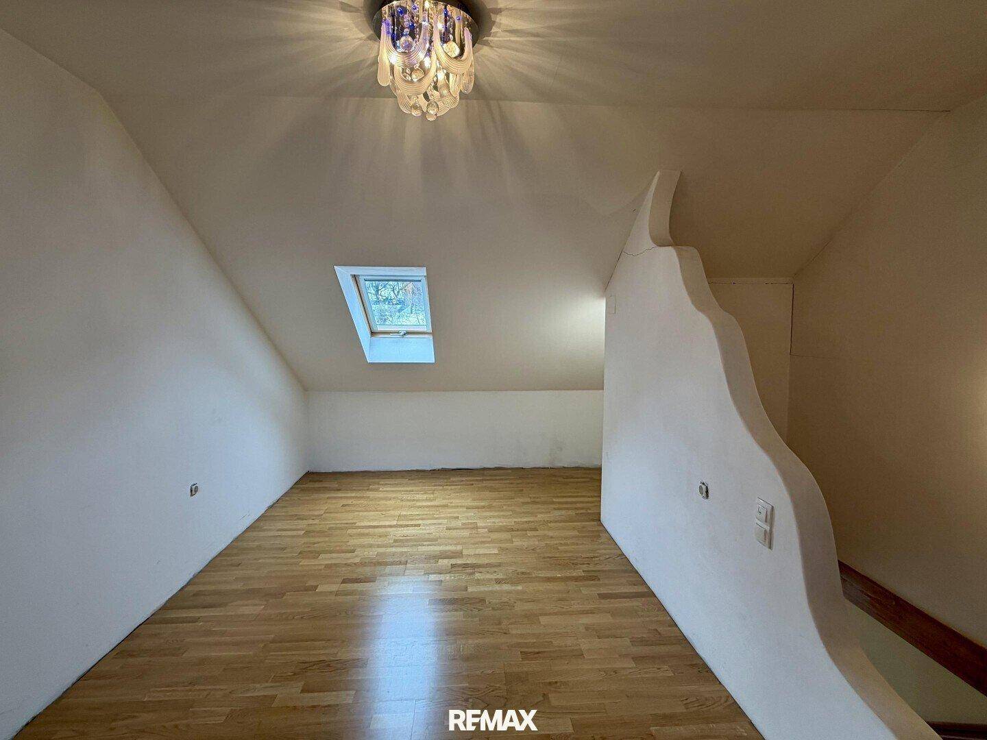 Dachgeschossraum mit Holzboden, Dachschräge und einem Dachfenster für natürliches Licht.
