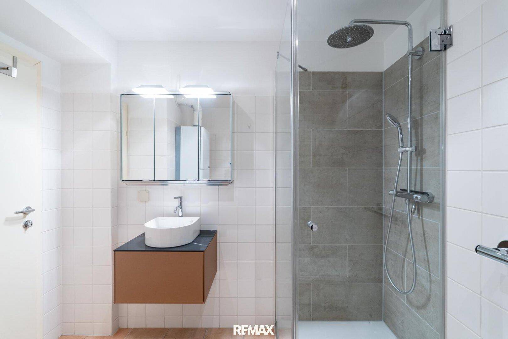 Modernes Badezimmer mit ebenerdiger Dusche, Regenbrause und stilvollem Waschbecken mit Spiegelschrank.
