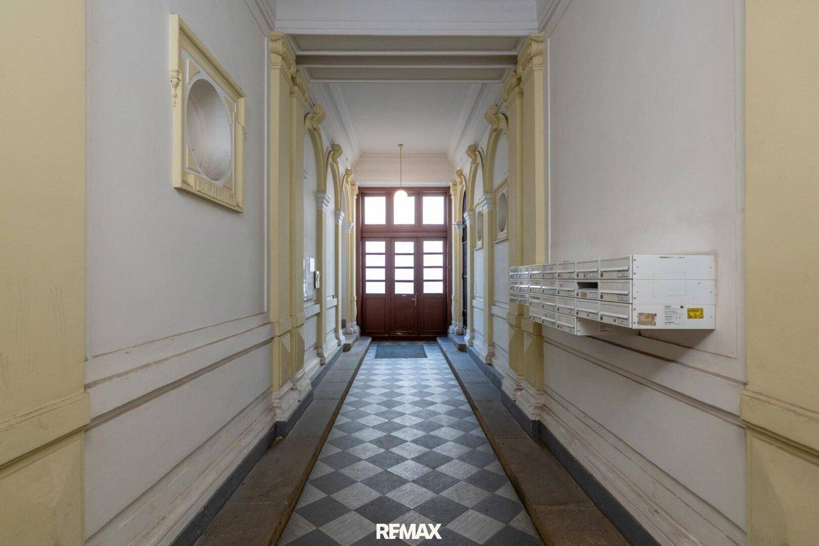 Historischer Hausflur mit Schachbrettmuster-Fliesen und dekorativen Wandelementen, klassischer Altbau-Charme.