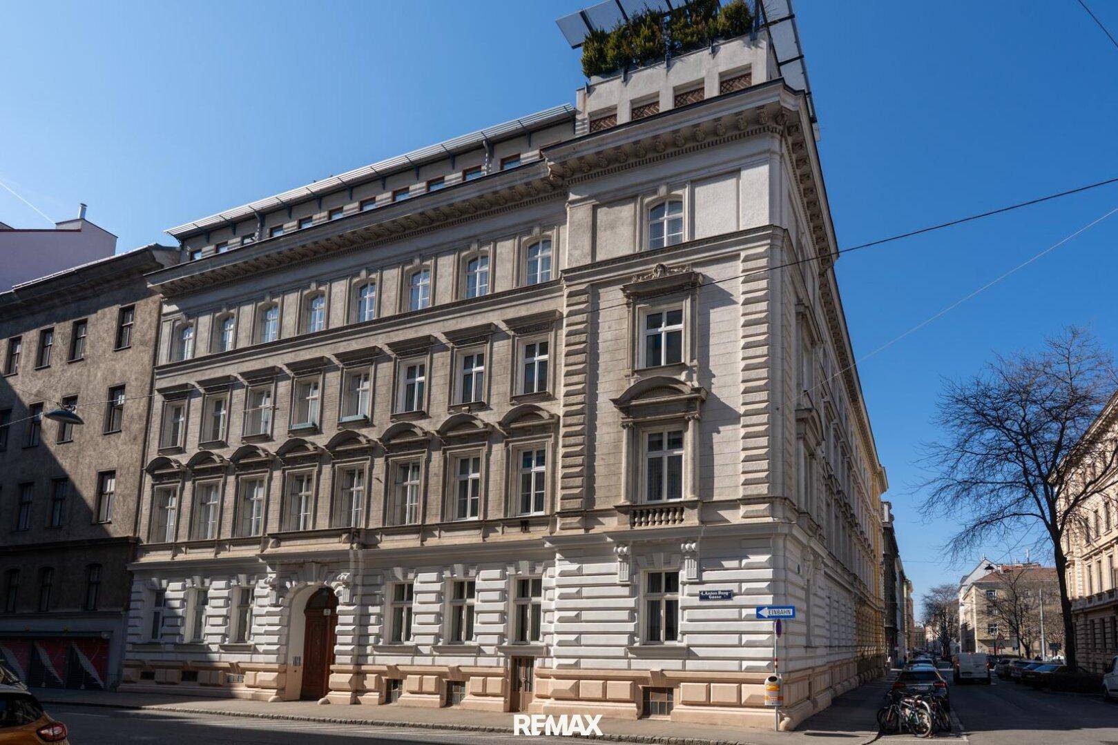Elegantes Altbaugebäude mit klassischer Fassade und Dachterrasse in urbaner Umgebung, sonniger Tag.