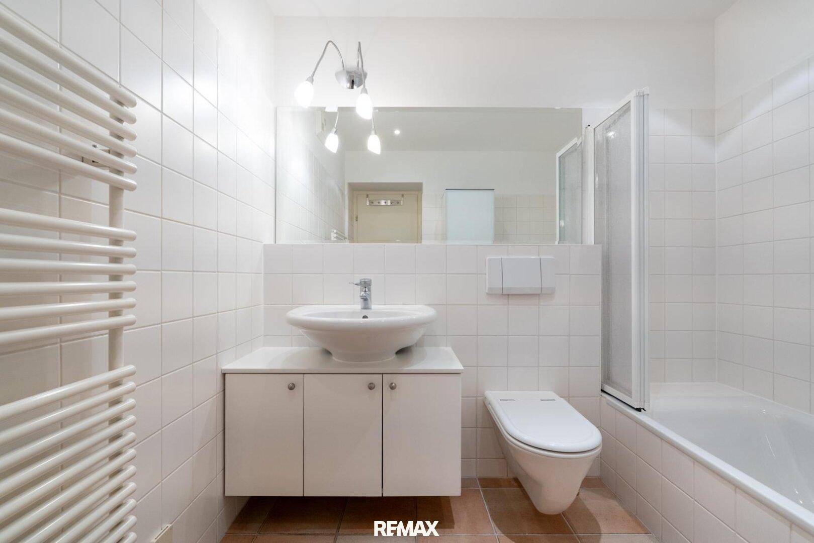 Helles Badezimmer mit Badewanne, WC, Waschbecken und beheiztem Handtuchhalter, funktional und sauber.