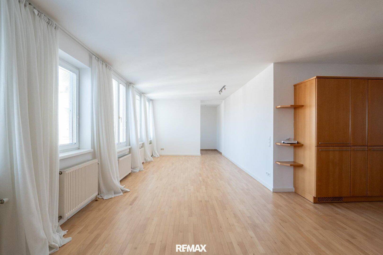Geräumiger, heller Wohnbereich mit vielen Fenstern und Holzfußboden, bereit zur Einrichtung.