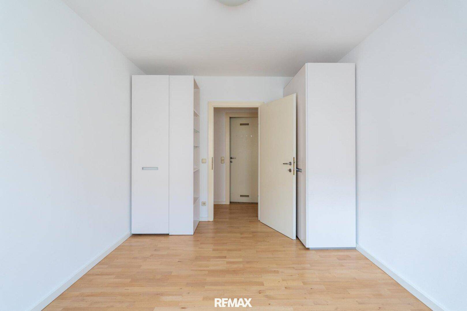 Schlafzimmer oder Ankleidezimmer mit weißen Einbauschränken und Parkettboden, hell und funktional.