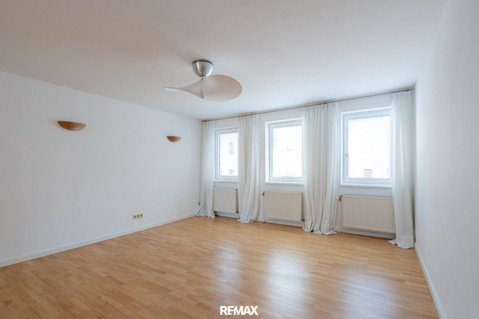 Helles Zimmer mit Holzfußboden, Deckenventilator und drei Fenstern, ideal als Schlafzimmer.