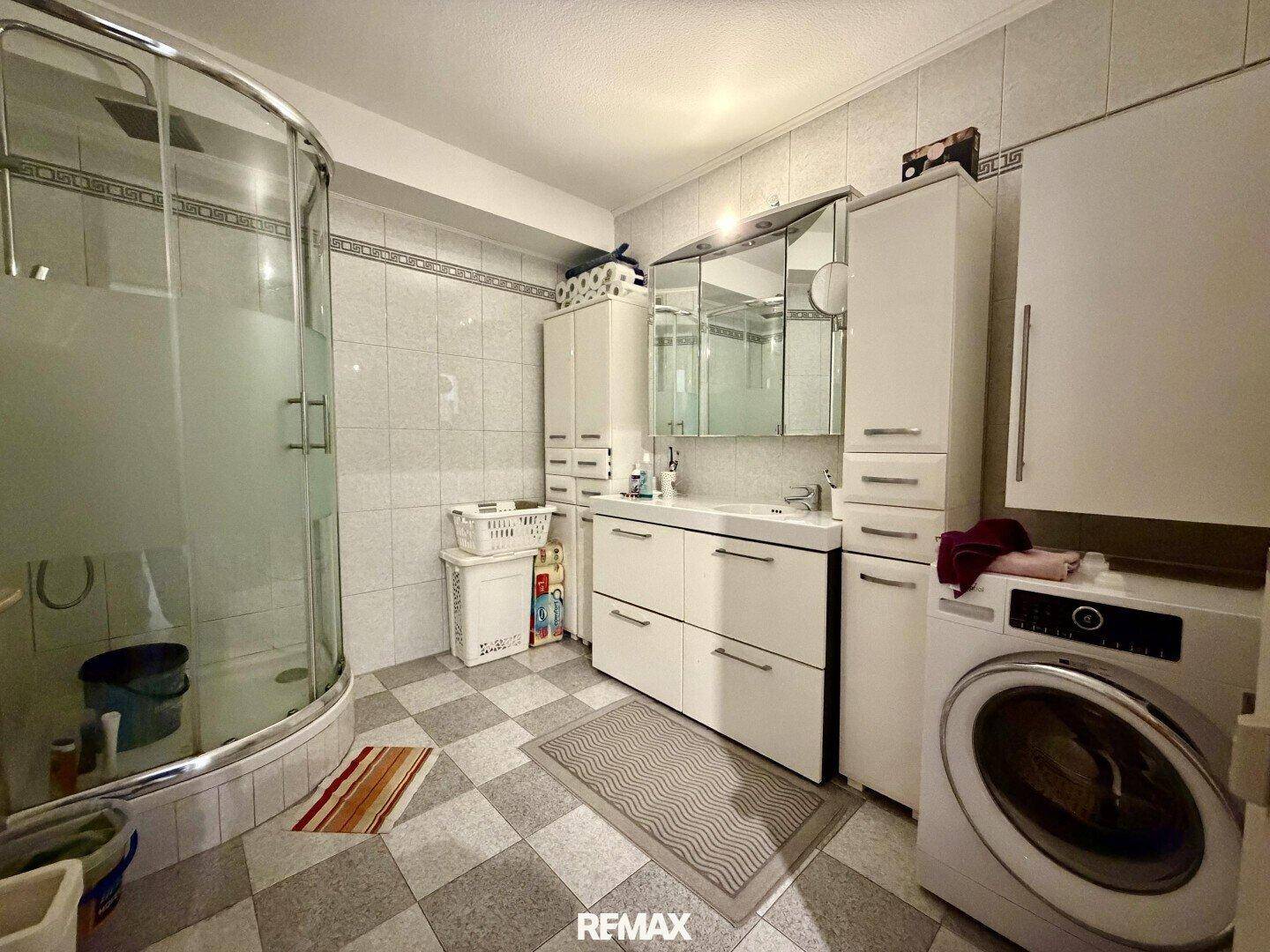 Badezimmer mit Duschkabine, Waschbecken, Spiegelschrank und Waschmaschine.
