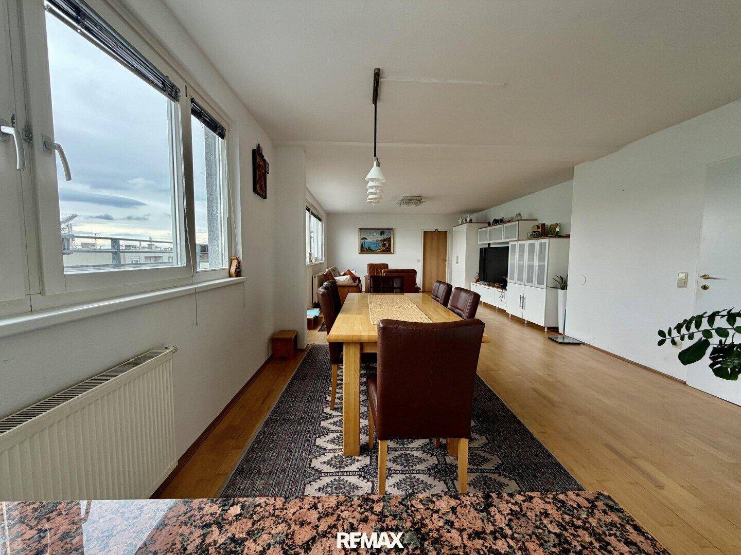 Heller Essbereich mit Holztisch und Blick auf den Wohnbereich und die Fensterfront.