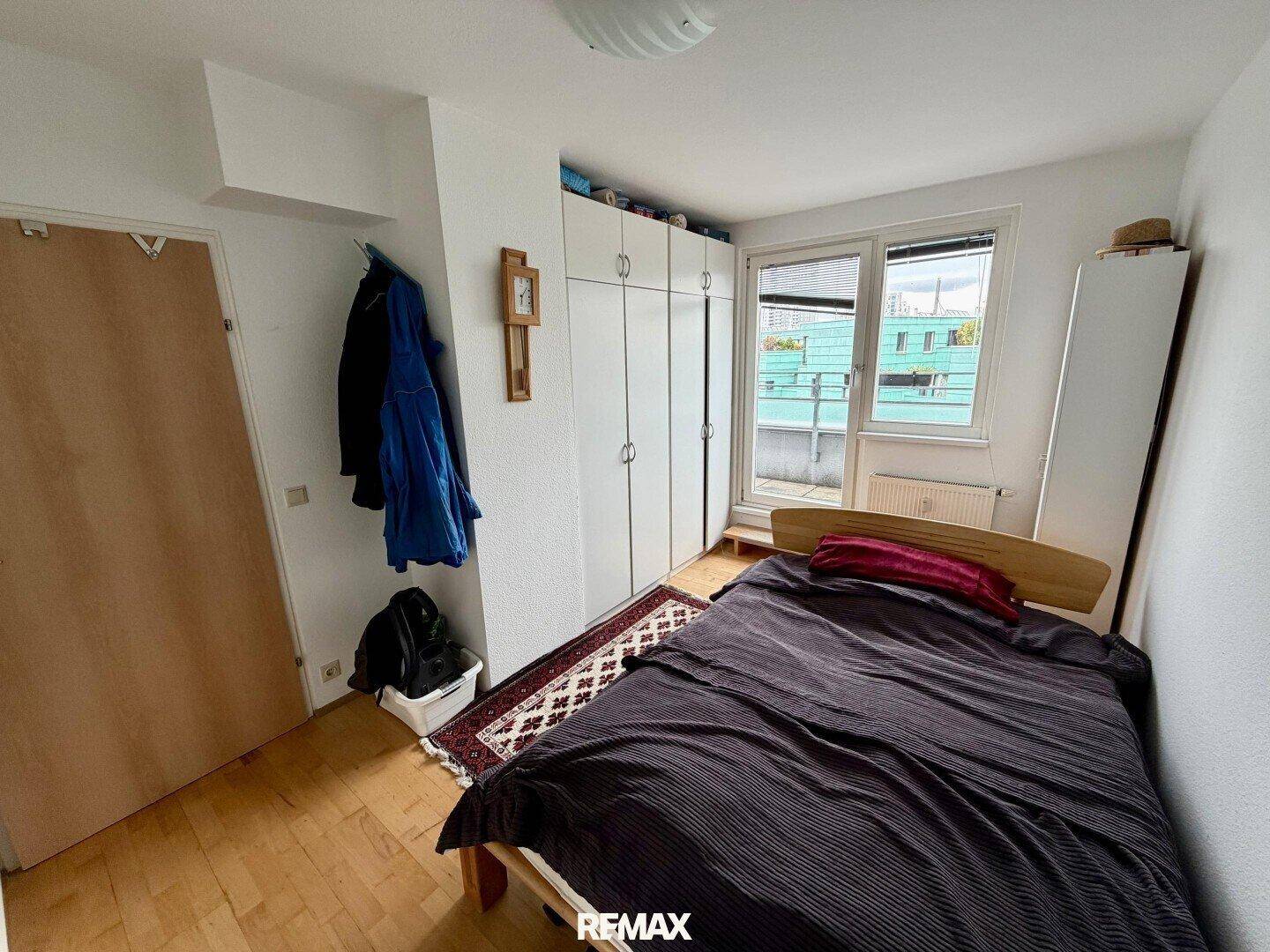 Schlafzimmer mit Holzboden, Einbauschränken und Zugang zu einem kleinen Außenbereich.