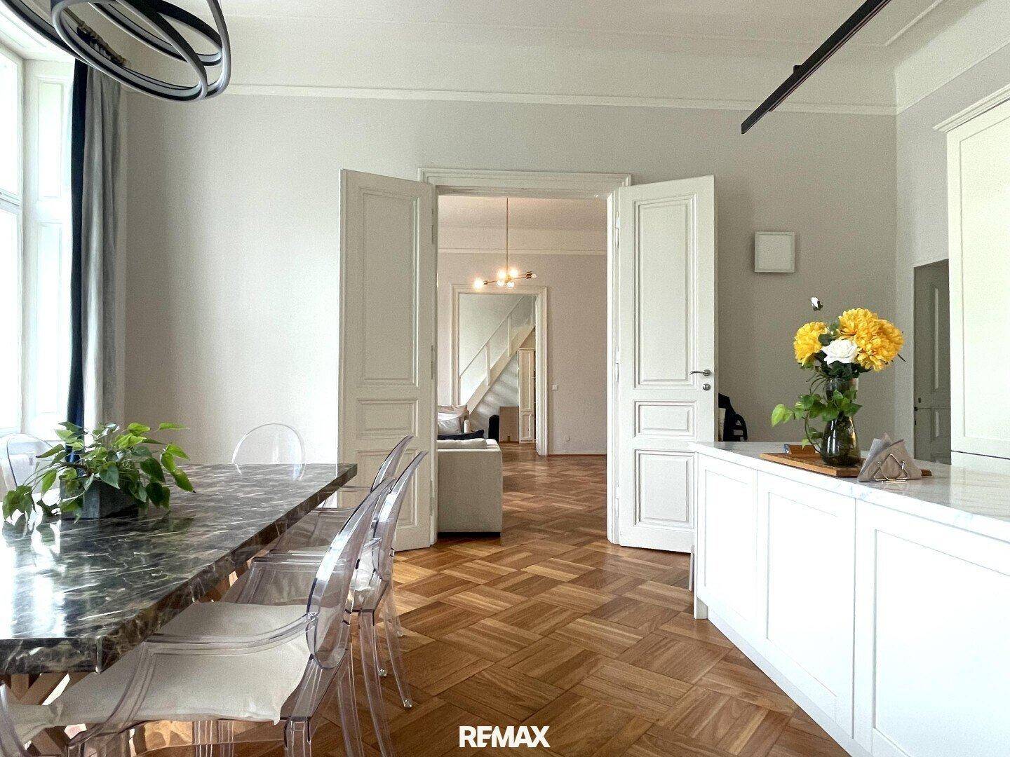 Eleganter Essbereich mit Marmortisch und Parkettboden, verbunden mit Küche und Wohnzimmer.