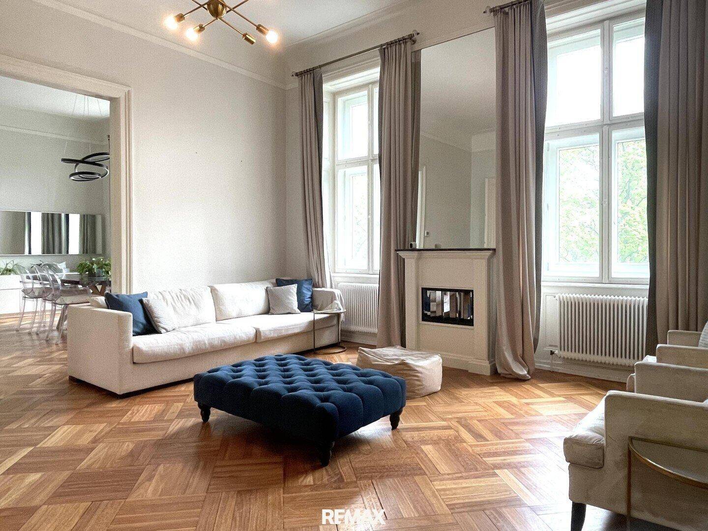 Helles Wohnzimmer mit bequemem Sofa, blauem Ottoman und dekorativem Kamin, Parkettboden.
