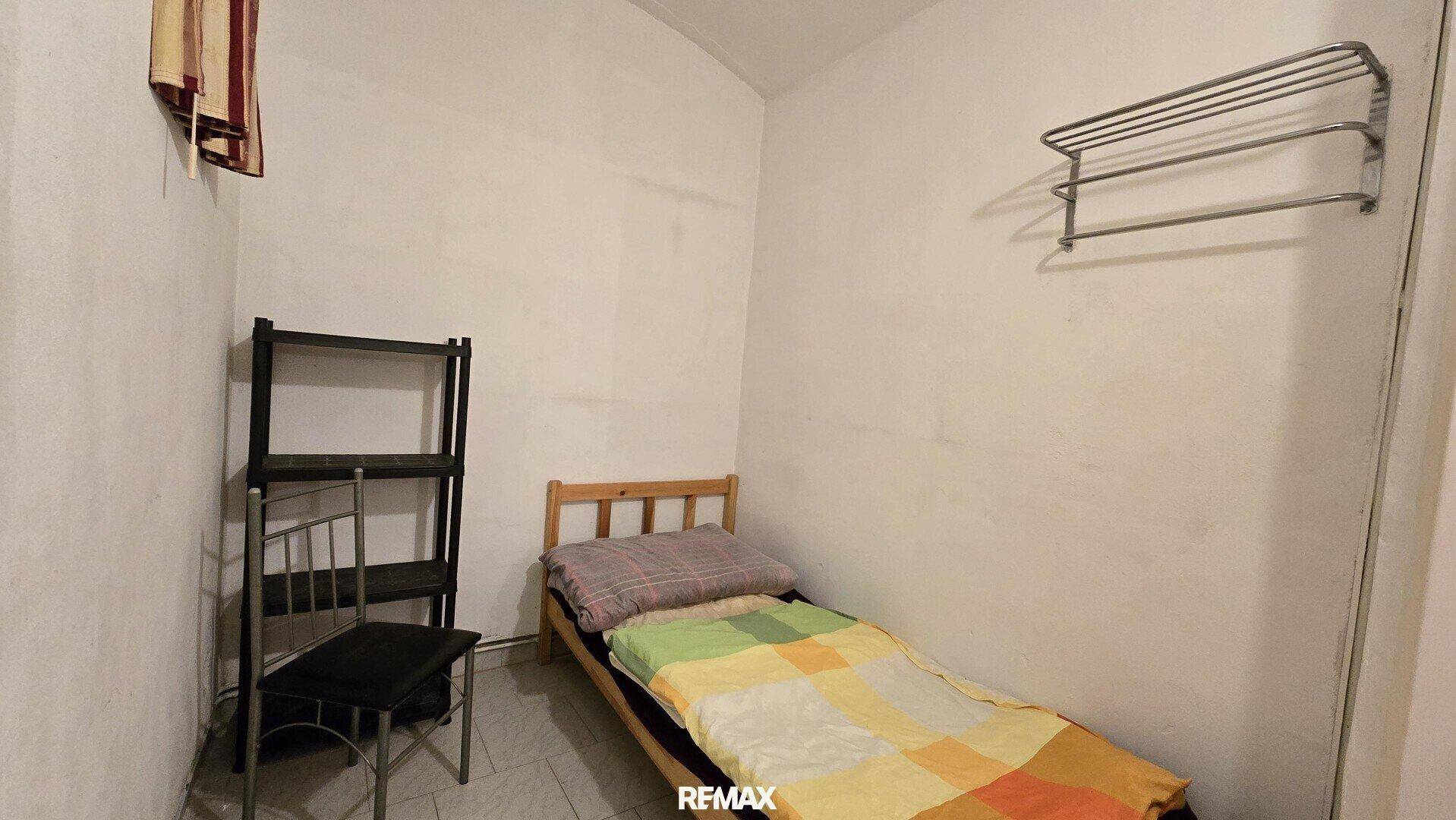 Einfaches Schlafzimmer mit Einzelbett, einem Regal und einem Handtuchhalter an der Wand.
