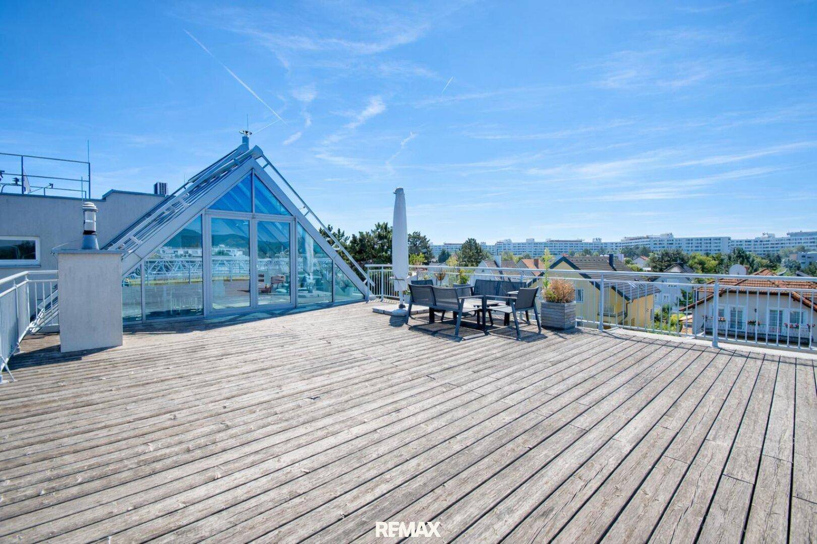 Weitläufige Dachterrasse mit Holzboden und moderner Glasstruktur, bietet einen weiten Blick über die Stadt.