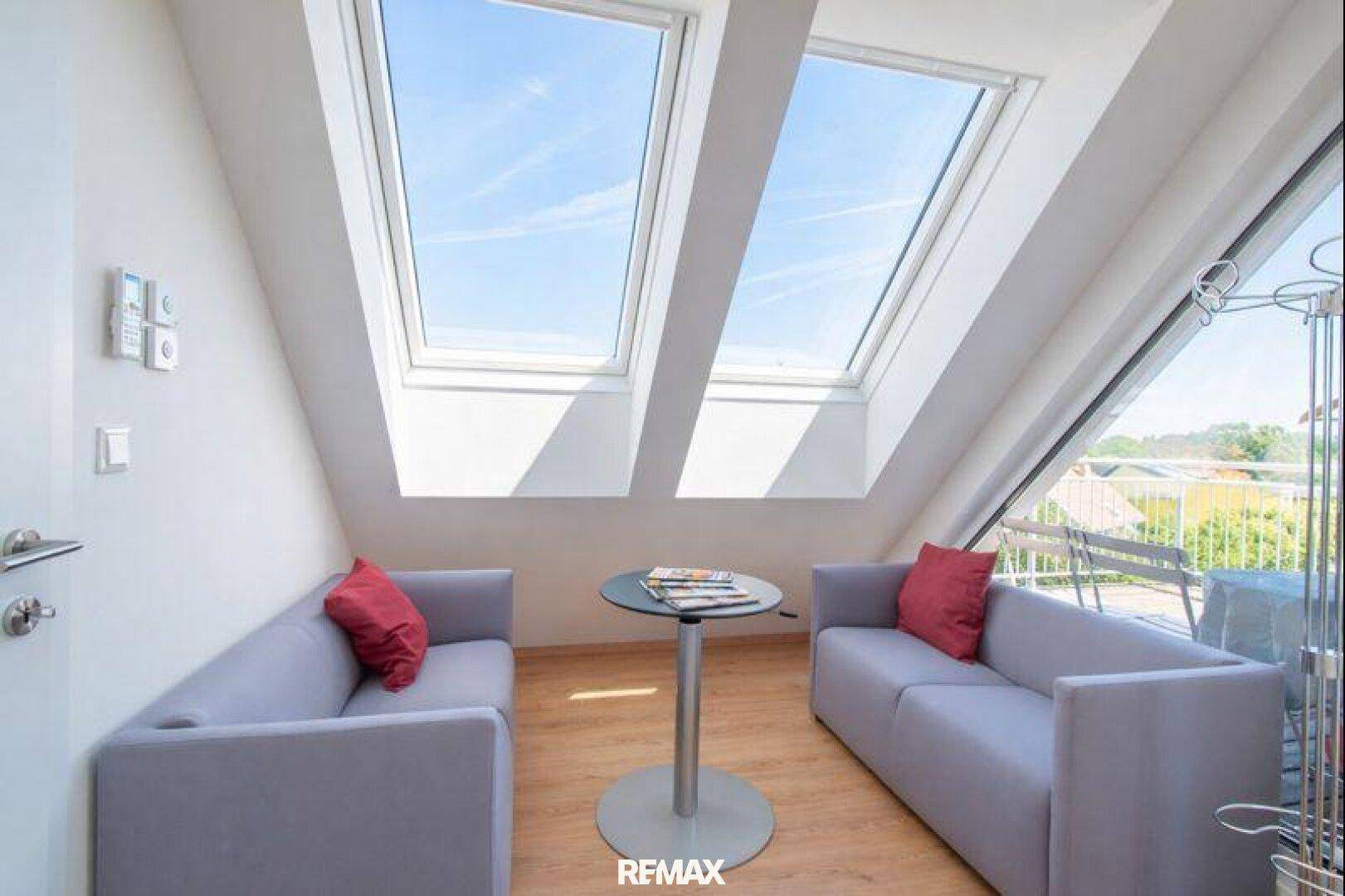 Kleiner, heller Wohnbereich mit zwei Sofas und großen Dachfenstern, die Zugang zum Außenbereich bieten.