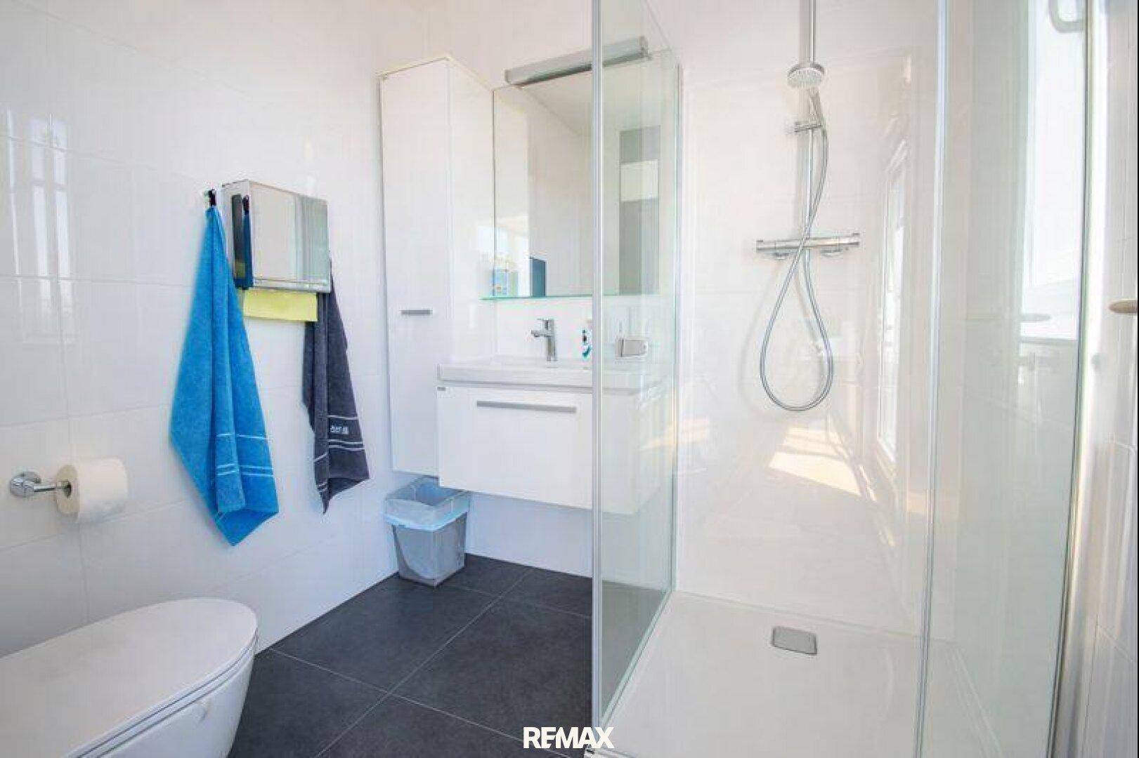 Modernes Badezimmer mit ebenerdiger Dusche, Hänge-WC und Waschtisch, in hellen und dunklen Fliesen.
