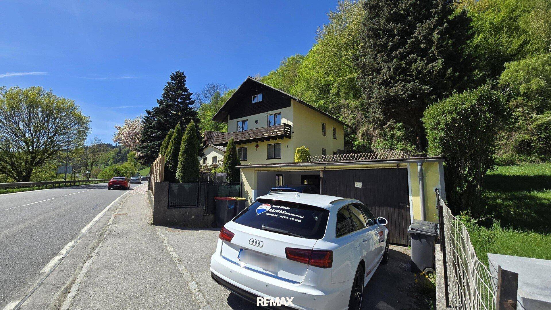Ansicht des Hauses von der Straße mit Garage und geparktem Auto, umgeben von viel Grün.